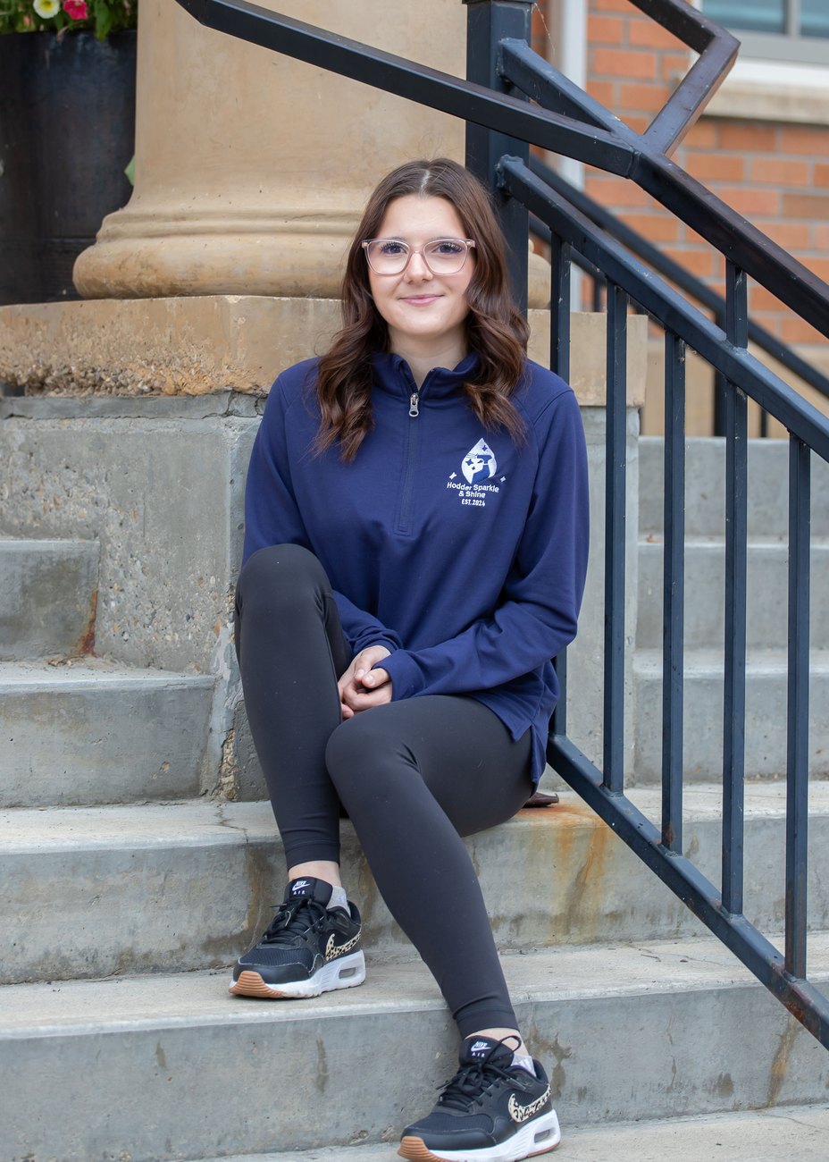 Gracie, Hodder Sparkle & Shine cleaner, sitting on steps in her HSS quarter-zip